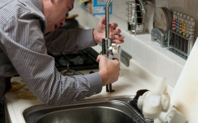 Geb&auml;udereinigung Berlin &ndash; Handwerker montiert eine Armatur an einem Edelstahlsp&uuml;lbecken